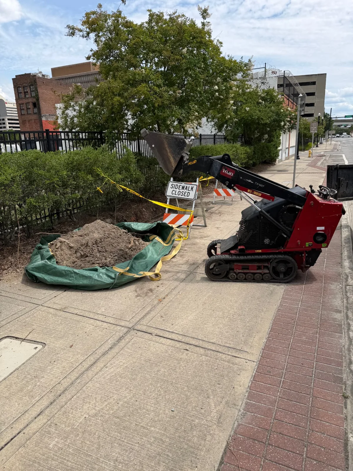 Compact track loader and dirt haul bag on a downtown Jacksonville sidewalk job site